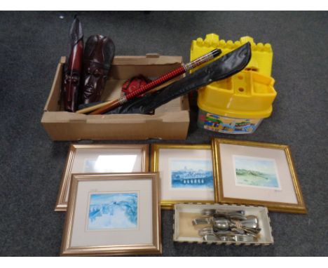 A box containing tribal masks, gilt framed Tom Macdonald print, two piece snooker cue, plated cutlery and MEGA blocks