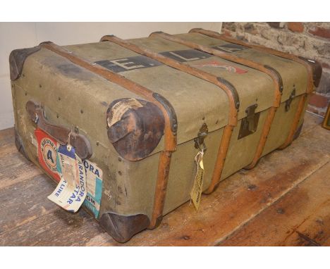 A large vintage canvas and wood bound travel trunk with re-enforced leather corners with some travel labels and initialed E L