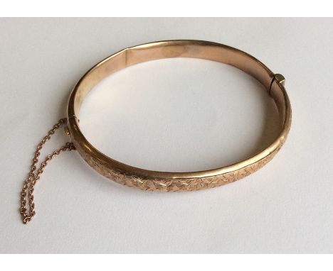 A 9 carat hinged bangle together with safety chain. Approx. 8 grams. Est. £50 - £80.