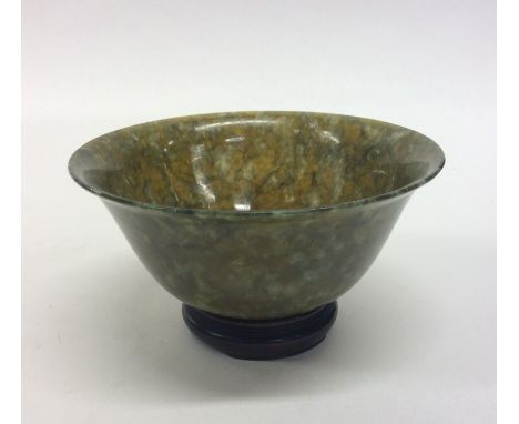 A small circular jade tea bowl on hardwood base. Est. £35 - £45.