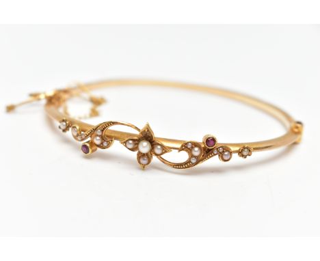 AN EARLY 20TH CENTURY 15CT GOLD BANGLE, a hinged bangle, decorated with a floral design, set with split seed pearls, and two 