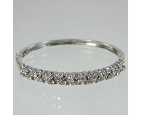 A modern 18 carat white gold and diamond set bangle, of hinged design, set with two rows of heart set stones, 6cm diameter