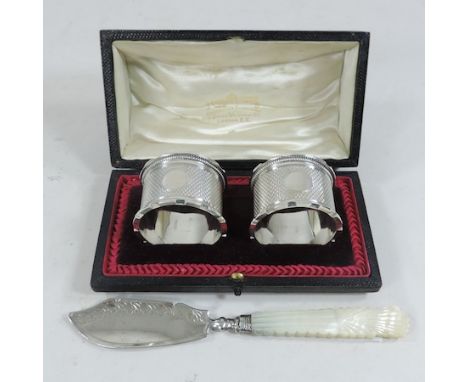 A cased pair of silver napkin rings, hall marked Birmingham 1906, together with a silver and mother of pearl slice 