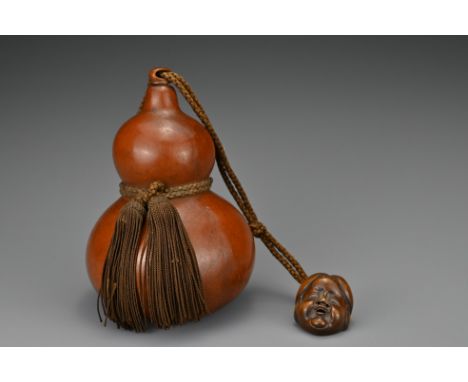 A Japanese double-gourd Hyotan sake flask with wooden stopper on rope tassels. Attached to the rope is a carved wooden netsuk