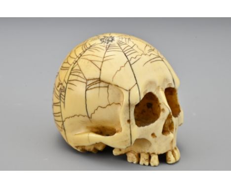 A Japanese ivory Netsuke in the form of a skull. The skull with incised decoration of a spiders web with spider and loose lea