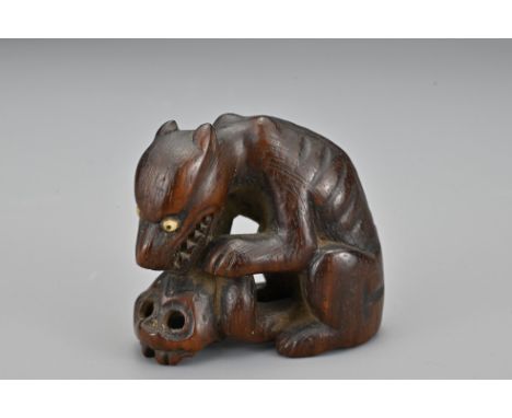 A Japanese carved wood netsuke in the form of a wolf with a skull. Signed to base. Meiji period. Height 4cm   Provenance: Pur