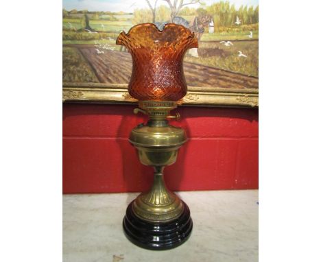 A brass based oil lamp with a pink/red scalloped floral form shade, black porcelain base 