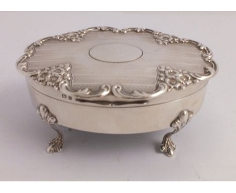 AN EDWARDIAN SILVER TRINKET OR JEWELLERY BOX of oval form with embossed floral and engine turned decoration, raised on four d