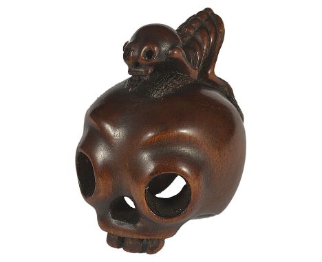 ˜A JAPANESE EBONY NETSUKE OF A SKELETON ON A HUMAN SKULL, EARLY MEIJI PERIOD, CIRCA 1880 the skull huge in comparison to the 