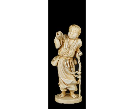 ˜A JAPANESE IVORY OKIMONO OF A YOUNG MAN, MEIJI PERIOD, LATE 19TH CENTURY standing in windswept robes leaning on a stick and 