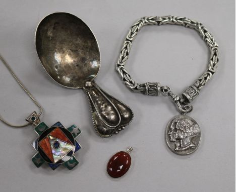 An Arts & Crafts white metal caddy spoon, a silver commemorative bracelet, a silver and enamel pendant & one other pendant.