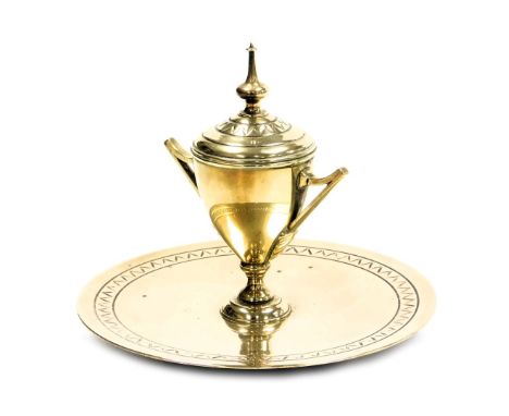 A Victorian brass inkwell, of trophy form, with a ceramic inset, raised on a circular base, 16.5cm wide.