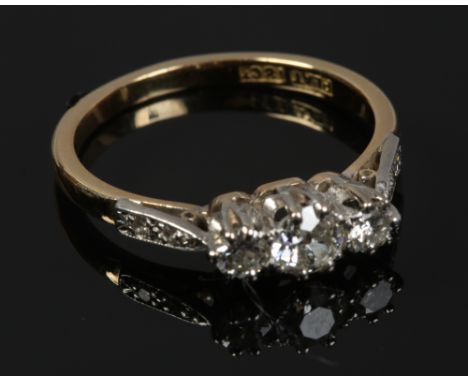 An 18ct gold and platinum three stone diamond ring with diamond set shoulders, size M1/2.