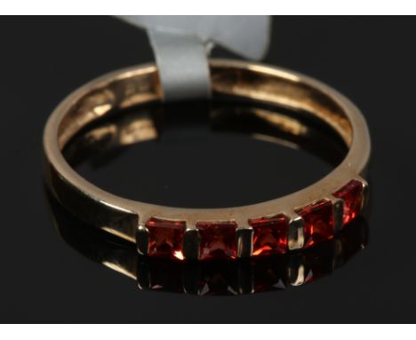 A 9ct gold dress ring with five Princess cut red / orange gemstones, size O.