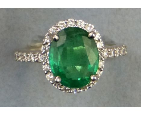 An emerald and diamond cluster ring, comprising central oval emerald (3.01ct) claw set over diamonds on an 18ct white gold sh