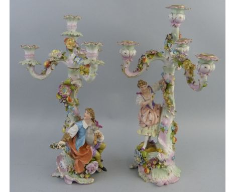 A near pair of continental figural candelabra, each with three branches and four sconces, encrusted with flowers and foliage,