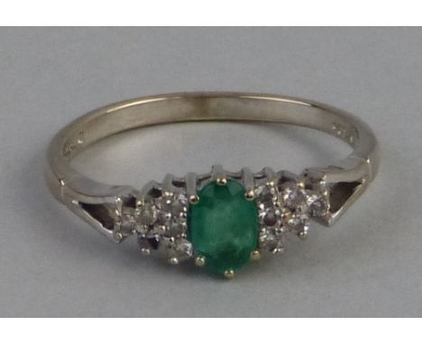 An emerald and diamond ring, comprising central oval emerald flanked to either side by six small diamonds set on 18ct white g