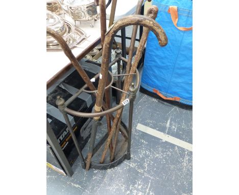 AN EDWARDIAN BRASS AND IRON STICK STAND CONTAINING A HORSE MEASURE WALKING STICK AND FOUR OTHERS.