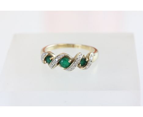 A 9 carat gold emerald and diamond ring, the three graduated round cuts with diagonal rows of brilliant cuts between, the eig