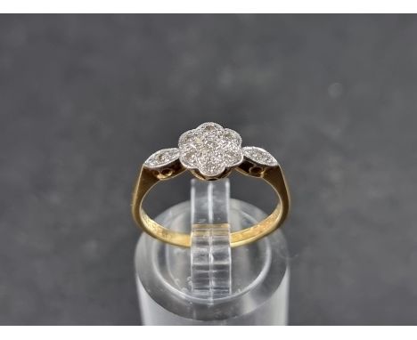 An 18ct gold daisy ring, set seven small diamonds with a further diamond to each shoulder, size M, gross weight 2.4g. 