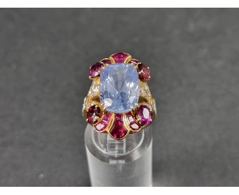 A yellow metal cocktail ring, set central blue topaz surrounded by rubies and diamonds, size K 1/2. 