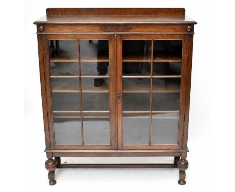 A 1920s oak two door display cabinet, with astragal glazed doors, on turned and block legs, height 127cm, width 106cm, depth 