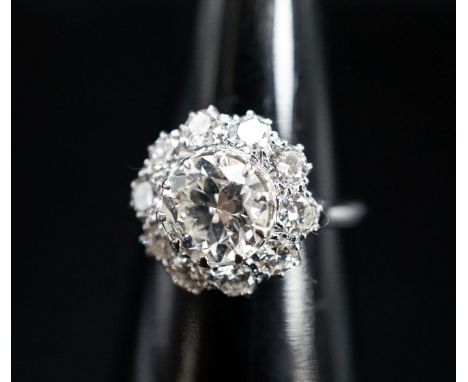 A white metal and eleven stone diamond set flower head cluster ring, the central stone weighing approximately 1.60ct, size N,