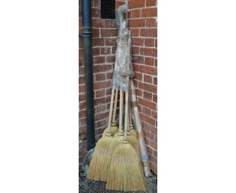 Seven wooden handled brooms with red bristles and two wooden hammer handles