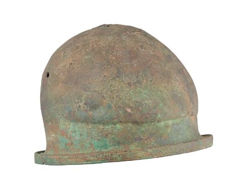 AN ITALIC BRONZE HELMET OF NEGAU TYPE, MID-5TH CENTURY B.C.  ‡ formed in one piece, the domed crown rising to a gentle medial