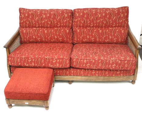 An Ercol wooden framed three seat bergere sofa and a matching footstool. Both raised on bun feet, the sofa upholstered in red