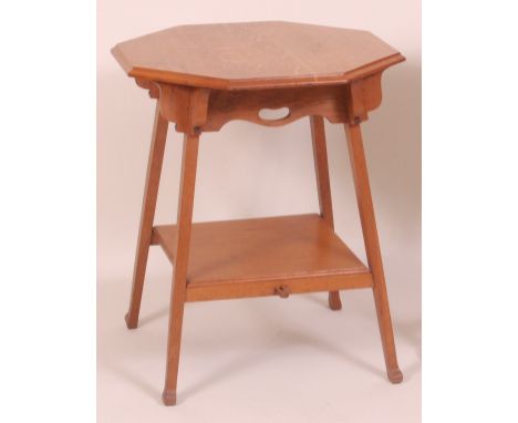 An Arts & Crafts light oak octagonal topped two-tier occasional table, having a shaped frieze and raised on rectangular cut t