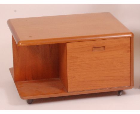 A 1970s teak coffee table, having fallfront cupboard door opposing single drawer and open compartments, on roller castors, h.