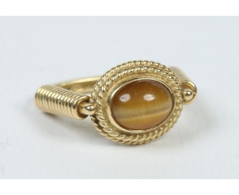 An 18 carat gold and cats eye Chrysoberyl designer ring set with an ovoid stone in a rope twist bezel over reeded shoulders, 