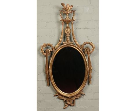 A 20th century neo Classical style giltwood oval hall mirror. Surmounted with an urn shaped finial and flanked with scrollwor