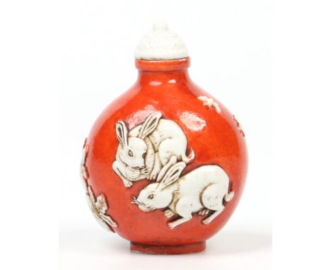 A Chinese porcelain snuff bottle and cover of globular form. Ground in red enamel and moulded in relief with a pair of rabbit