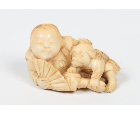 A Japanese Meiji period carved ivory netsuke. Formed as a reclining man holding a fan and with a puppy dog at his side clad i