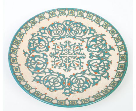 An Arts & Crafts terracotta charger. Cream ground and glazed in tones of green and orange with stylized strapwork. Label for 