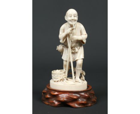 A Japanese Meiji carved ivory Okimono on hardwood plinth. Formed as an elderly man smoking a pipe resting from harvesting fru