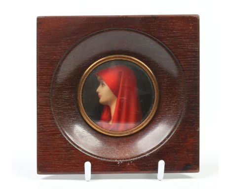 An early 20th century framed portrait miniature of a young woman wearing a red hood, 6cm diameter.  Condition Report. To be u