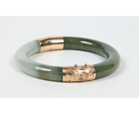 A Chinese mottled spinach and celadon jade bangle with engraved 14 carat gold mounts, 8.25cm wide. Condition Report. To be us