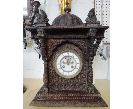 An Indian/Asian carved wooden mantel clock, early 20th century, with domed finial flanked by gargoyle type figures, the ename