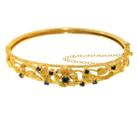 A SAPPHIRE SET 9CT GOLD BANGLE, OF OPENWORK FLORAL DESIGN WITH PLAIN LOWER HALF, 13G 