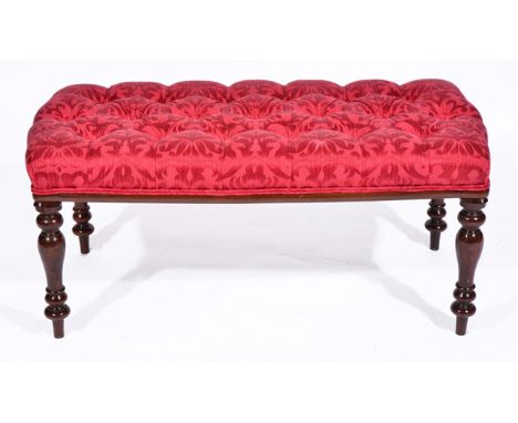 A MAHOGANY FRAMED STOOL with overstuffed button upholstered seat in red material, standing on turned tapering legs 102cm wide