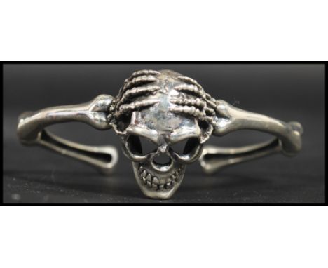 A sterling silver bangle bracelet in the form of two arms holding a skull. Weighs 38.6 grams measures 3 inches wide.&nbsp;