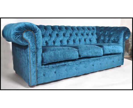 A contemporary Chesterfield button back large sofa settee upholstered in a blue crushed velvet with scrolled arms. Measures 7