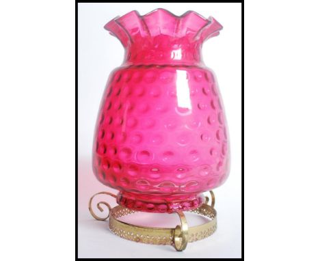 A 19th century Victorian cranberry glass oil lamp shade in the form of a pineapple with an undulate rim raised on a gilt scro