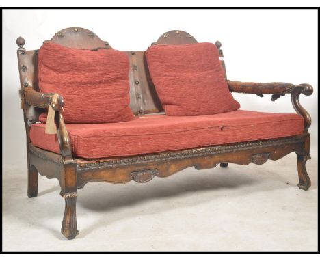 A 1920's Carolean revival beech wood and leather 2 seat sofa settee. Raised on shaped paw feet with studded leather and horse