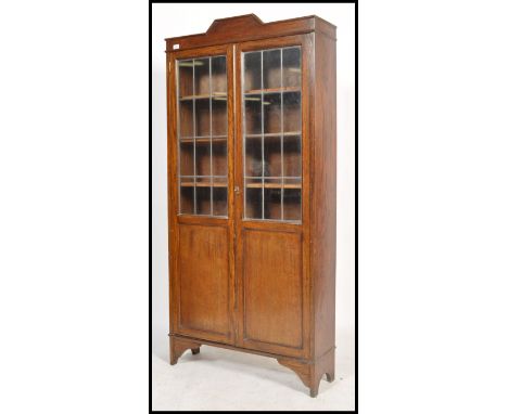 An early to mid 20th century glazed bookcase upright cabinet, fitted full length leaded glass and panel doors opening to reve