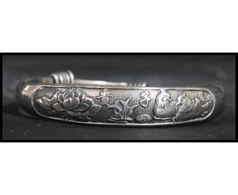 A Chinese silver bangle bracelet having an adjustable size with 'lucky' decoration with symbols lotus flower and birds. Weigh