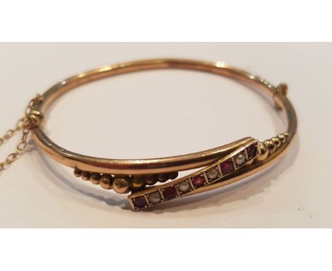 A Victorian 9ct gold, ruby and pearl channel set ladies bangle bracelet complete with the safety chain. Total weight 5.4g